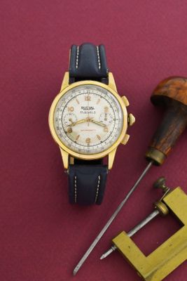 une montre en or et les outils d'un horloger posés sur un fond rouge