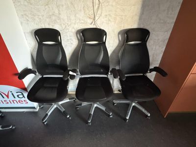 four black office chairs are lined up against a wall