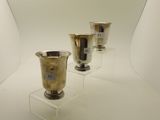 trois vases en argent exposés dans une pièce blanche