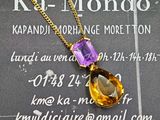 pendentif en cristal jaune et violet, monté sur une chaîne en or, présenté sur une carte de visite
