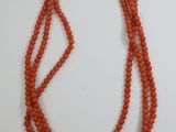 an orange beaded necklace with a gold clasp on a white background