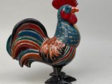 une figurine de coq aux couleurs vives posée sur une surface blanche
