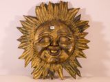 a gold sun face hanging on a white wall