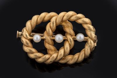 a close up of a gold and pearl broochle on a black surface