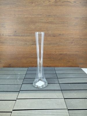 un vase en verre posé sur un sol carrelé, près d'un mur en bois