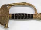 a gold sword with a black handle on a white surface