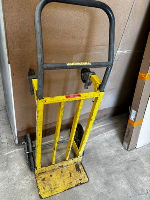 un diable jaune muni d'une poignée noire, à côté d'un carton