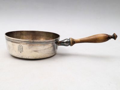 une vieille casserole en argent avec un manche en bois, posée sur une surface blanche