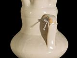 a white vase with a bird sticking out of it ' s side