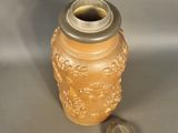 a brown vase with a silver lid next to a coin
