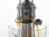 un extracteur de jus à côté duquel se trouve un verre de jus d'orange
