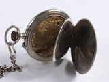 a silver pocket watch with a chain on a white surface