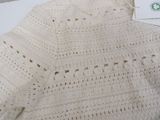 a white crocheted sweater on a bed with a tag