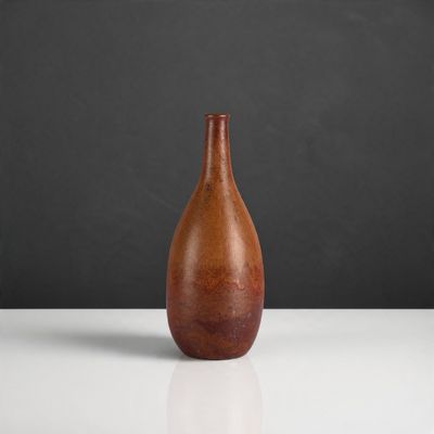 un vase orange posé sur une table blanche, près d'un mur noir
