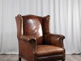 une image représentant un fauteuil en cuir marron posé sur un parquet en bois massif