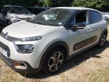 une petite voiture blanche garée dans un champ, avec d'autres voitures en arrière-plan