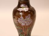 a brown vase with purple flowers on it on a white surface