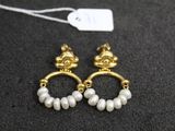 une paire de boucles d'oreilles en or et perles posées sur un fond noir
