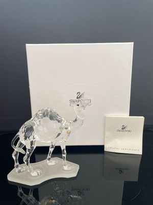 figurine en cristal représentant un chameau posée sur une table noire, à côté d'une boîte blanche