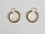 une paire de boucles d'oreilles créoles en or posées sur une surface blanche