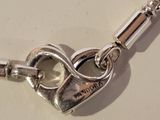 silver heart shaped pendant with a chain attached to it on a white surface