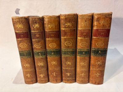 six old books are lined up in a row on a white surface