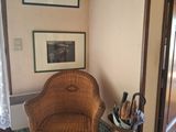 une chaise en osier dans un coin d'une pièce où sont accrochés des tableaux au mur