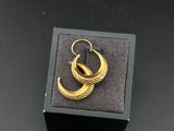 une paire de boucles d'oreilles en or dans un écrin noir posé sur une surface noire