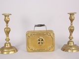 two gold candlesticks and a suitcase on a white surface