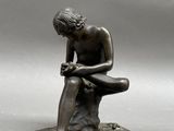 bronze statue of a man sitting on a rock with his hands on his knees