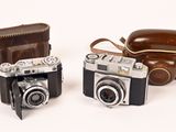 two old cameras sitting next to each other on a white surface