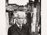 black and white photograph of a man in a suit standing in front of a building