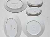 four white plates on a white table with a clock on one of them