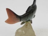 statue of a fish sitting on top of a rock on a white surface