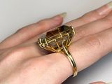a woman ' s hand holding a gold ring with a brown stone