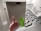 a white shelf with a pink dust pan, a green cup, and a pink dustpant on it