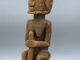 une statue en bois représentant une personne assise sur une chaise