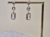 silver square earrings on a gold stand on a marble table