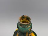 un vieux vase vert et jaune posé sur une table blanche