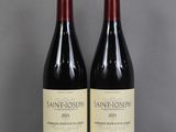 Deux bouteilles de vin sont posées sur une table en verre devant un mur gris.
