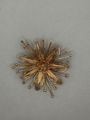a gold flower brooch on a white surface