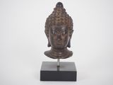 a bronze head of a buddha on a black stand