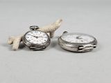 two silver pocket watches sitting next to each other on a table