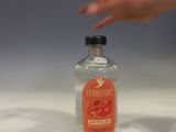 a bottle of alcohol sitting on a counter with a hand reaching for it