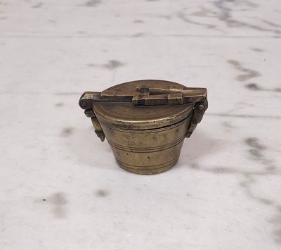 an old brass container with a handle sitting on a white surface