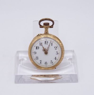 une petite montre de poche en or posée sur un socle transparent