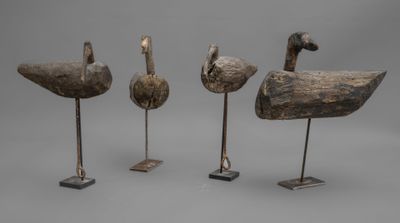 trois canards en bois sculptés posés sur des socles, sur fond gris