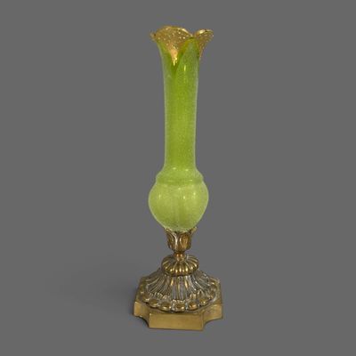 un vase ancien en verre vert posé sur un socle doré, sur fond gris