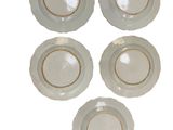 four white plates with gold rims are arranged on a white surface