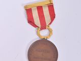 an old medal on a white surface with a red and white stripe ribbon